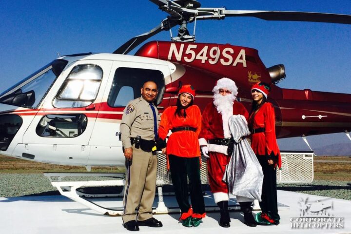 Santa, 2 helpers, and a CHP officer stand in front of a helicopter