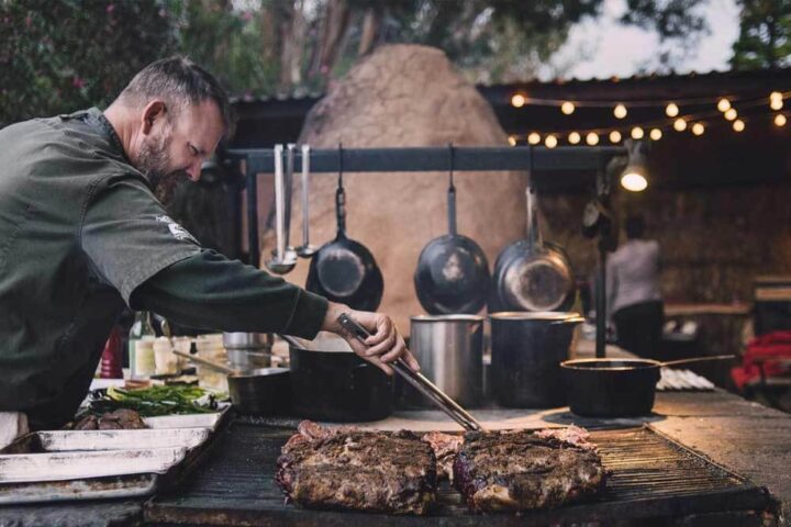 Chef cooking meat on a grill at Deckman’s En El Mogor