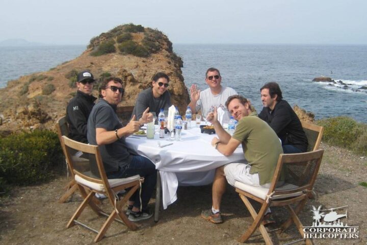 A group of people a table on a cliff overlooking the ocean
