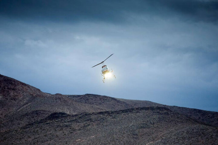 A helicopter with spotlight on flies over desert terrain