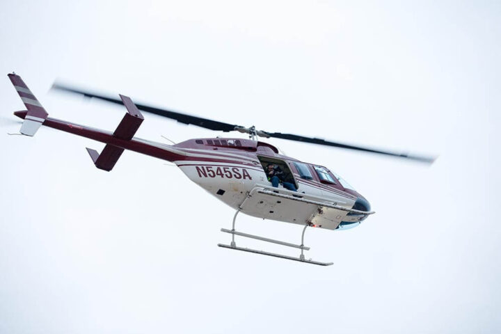 A helicopter in flight viewed from below, a photographer can be seen in the open door