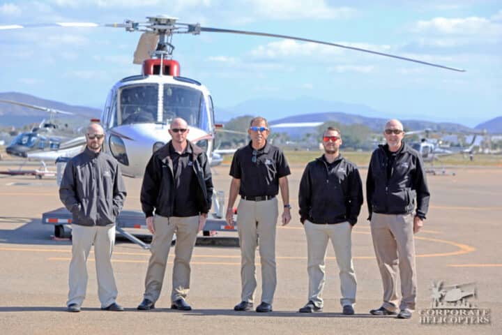 5 men stand in front of a helicopter
