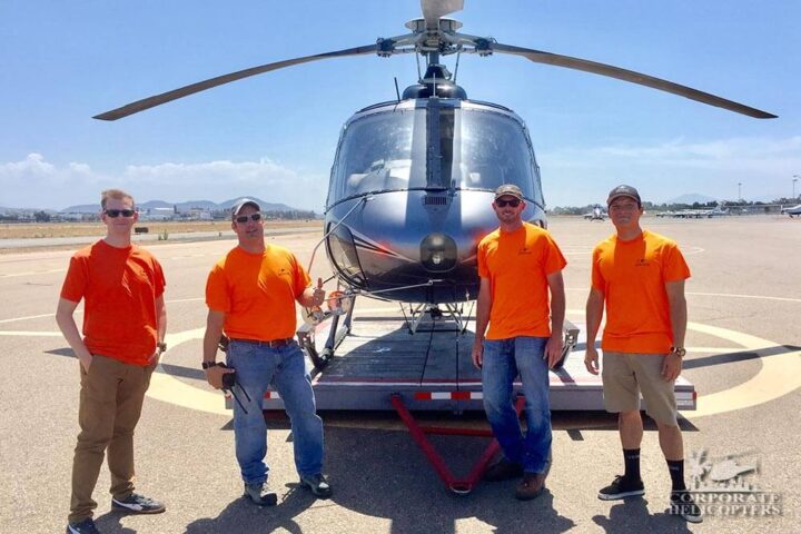 4 men in bright orange shirts stand in front of a helicopter