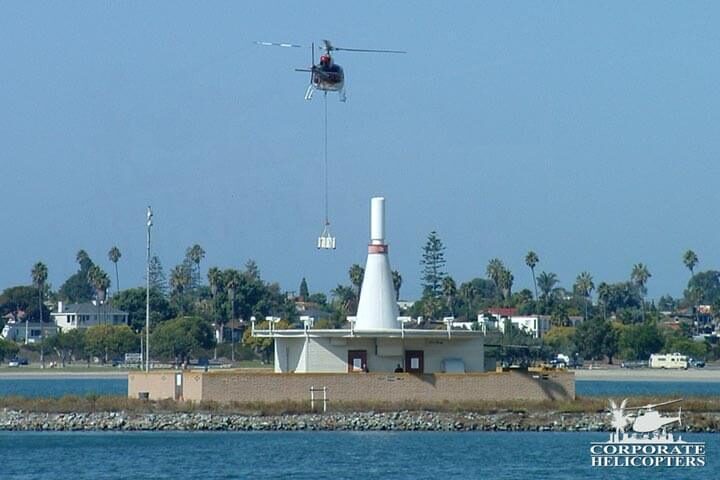 A helicopter carrying an external load by long line flies behind the bowling pin building in Mission bay