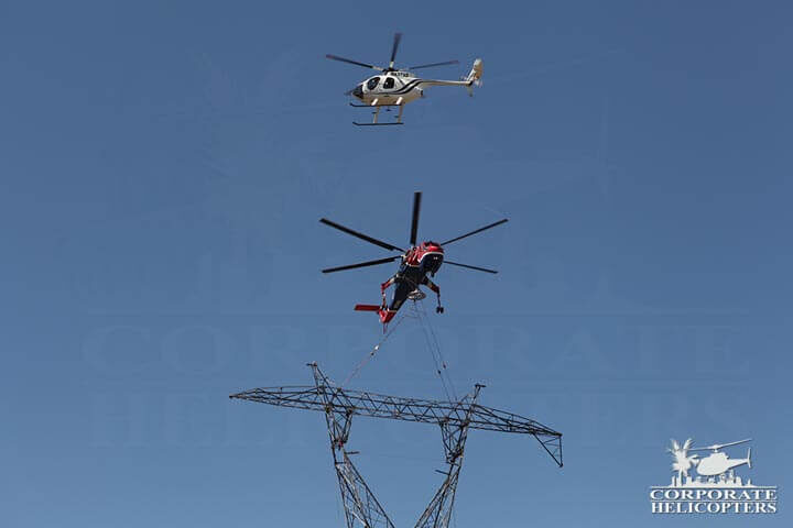 A helicopter flies over another helicopter that is lifting a large piece of equipment