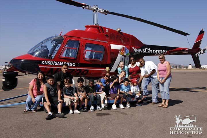 A class of teachers and kids stands in front a helicopter