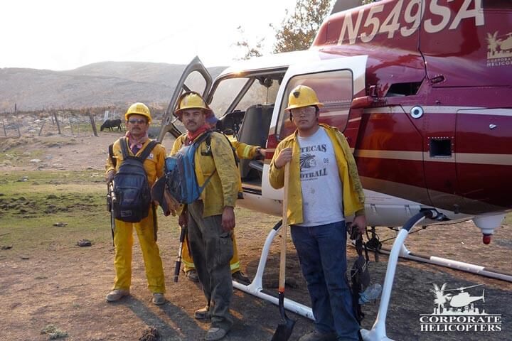 3 men with hardhats stand next to a helicopter
