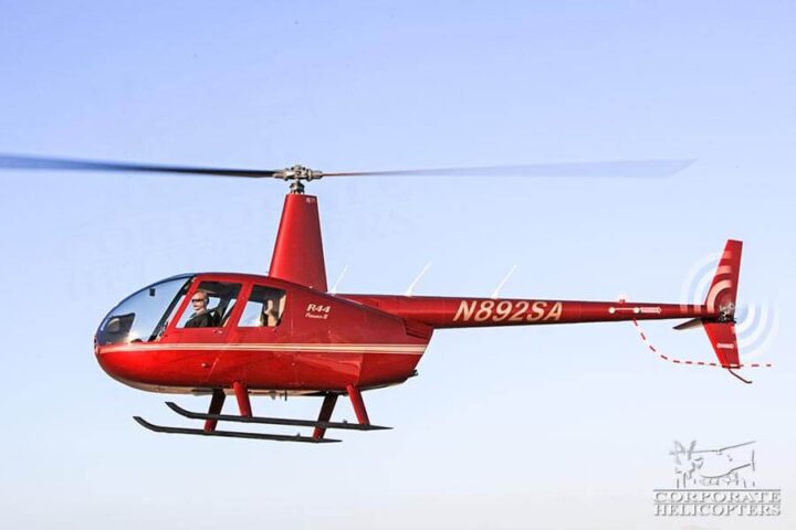 A red Robinson R44 Raven II helicopter in flight