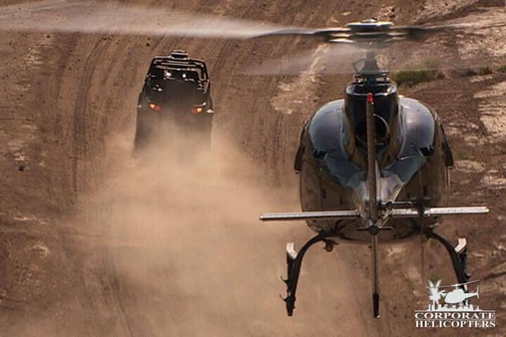 A helicopter chases an off road race vehicle in the desert