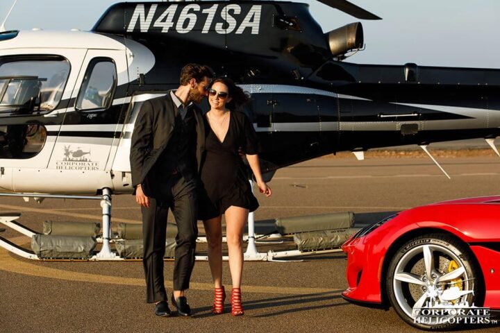 A well-dressed couple exits a helicopter and walks toward a Ferrari