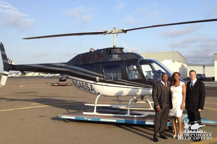 A wedding couple and another man pose in front of a helicopter