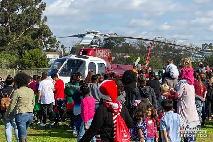 A large group of children and adults stand in front of a helicopter