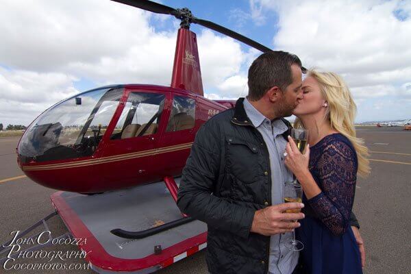 A newly engaged couple kiss in front of a helicopter