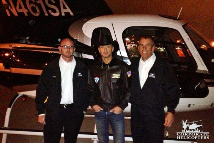 Tim McGraw and 2 pilots stand in front of a helicopter